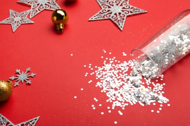 Photo of Composition with shiny confetti spilled out of champagne glass near Christmas decorations on red background, closeup