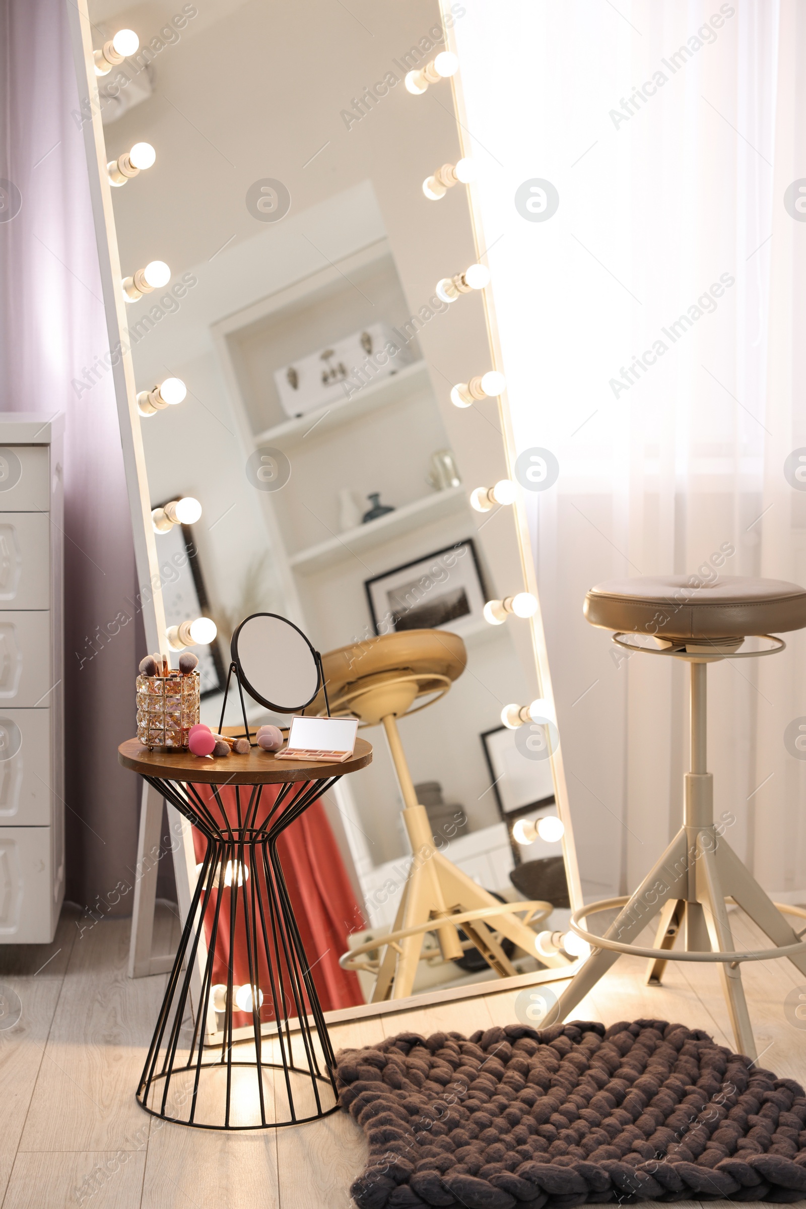 Photo of Makeup room. Stylish mirror with light bulbs, beauty products on table and chair indoors