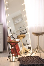 Makeup room. Stylish mirror with light bulbs, beauty products on table and chair indoors