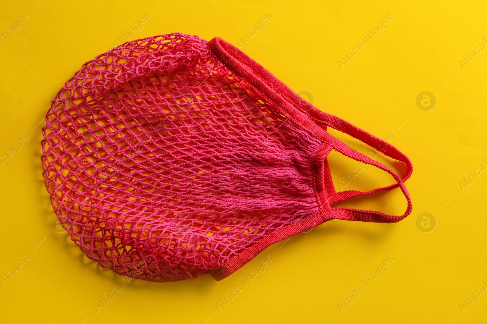 Photo of Empty pink net bag on yellow background, top view