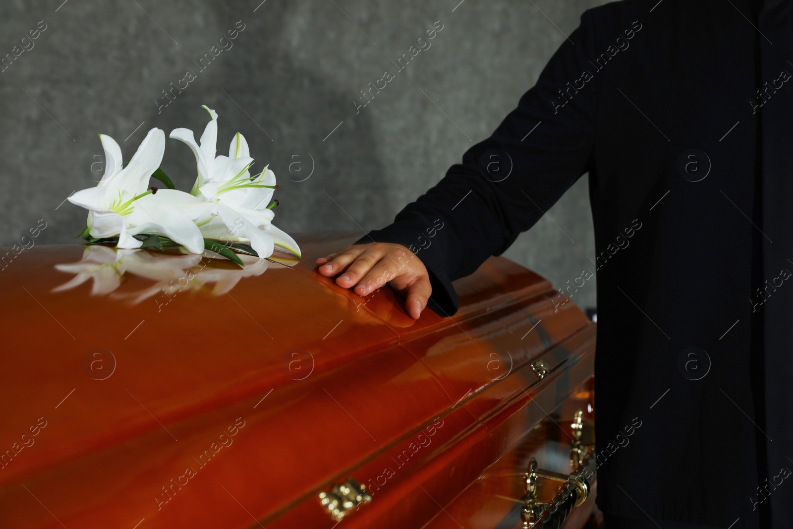 Photo of Young man near casket with white lilies in funeral home