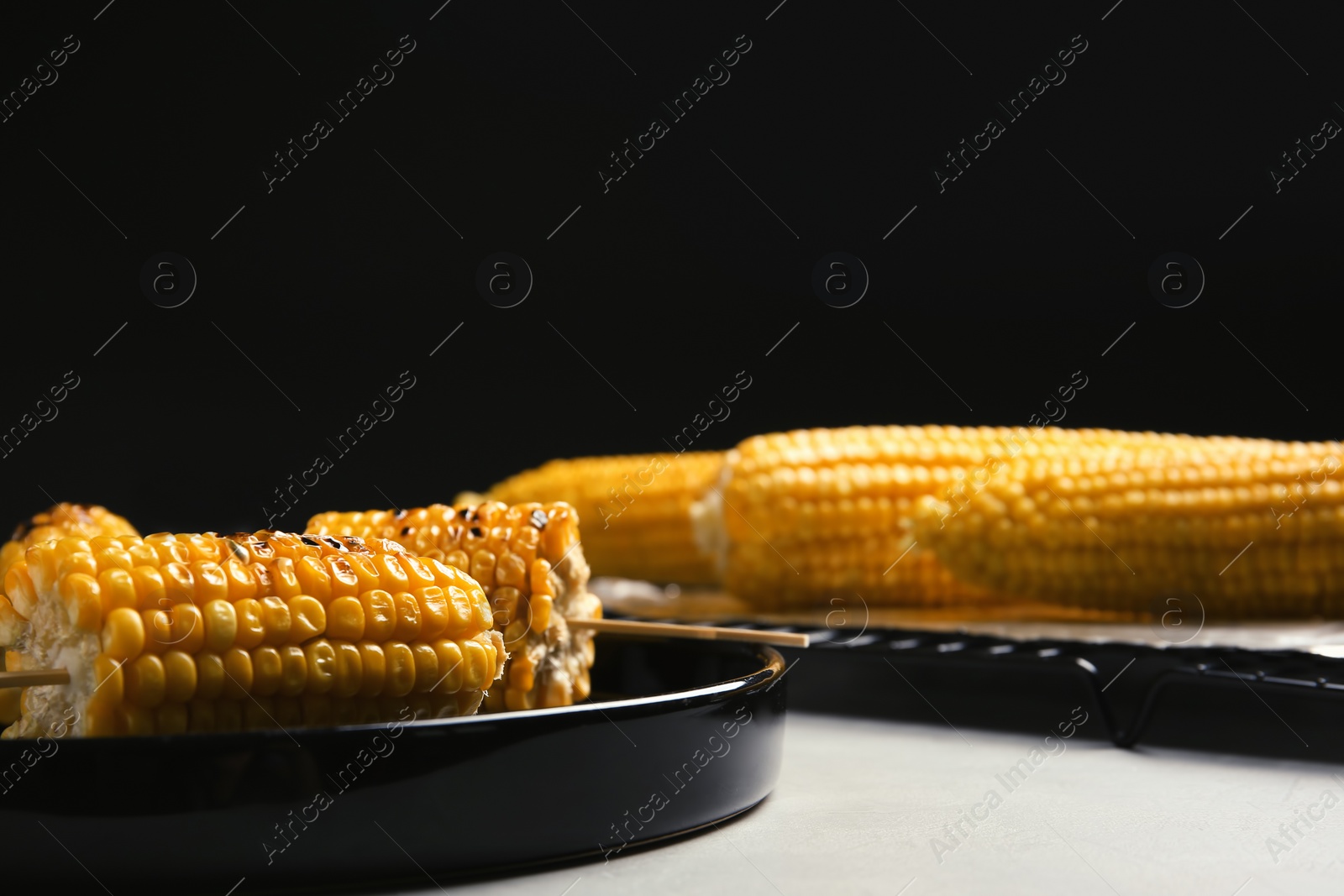 Photo of Ceramic plate with grilled corn cobs on light table. Space for text