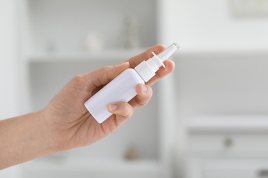 Photo of Woman holding nasal spray bottle indoors, closeup