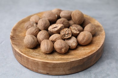 Wooden board with nutmegs on light grey table, closeup
