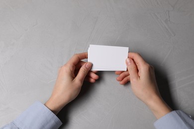 Photo of Woman holding blank cards at light grey table, top view. Mockup for design