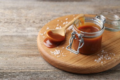 Jar and spoon with tasty salted caramel on wooden table, closeup. Space for text