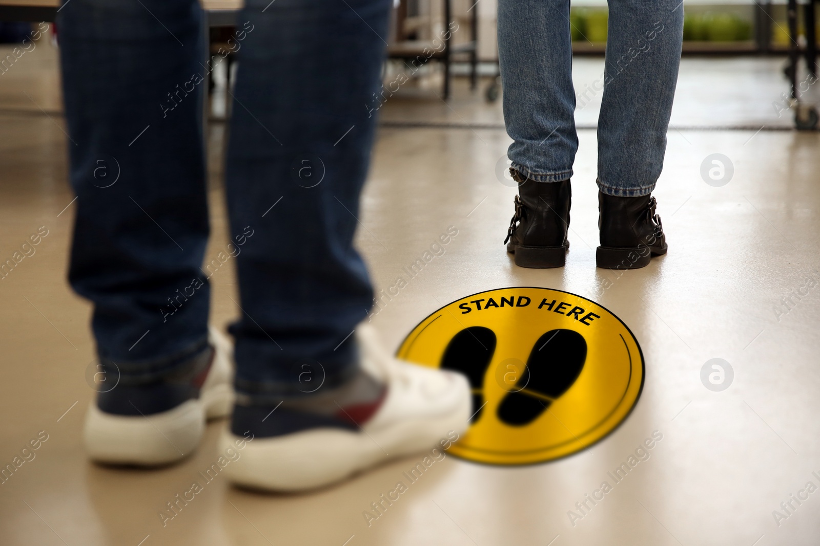 Image of Keep social distance as preventive measure during coronavirus outbreak. Yellow warning sign on floor between people, closeup