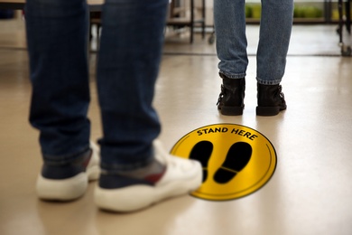 Image of Keep social distance as preventive measure during coronavirus outbreak. Yellow warning sign on floor between people, closeup