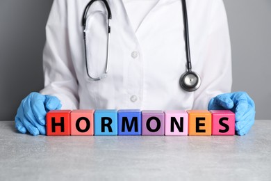 Photo of Doctor near word HORMONES made with colorful cubes at grey table, closeup