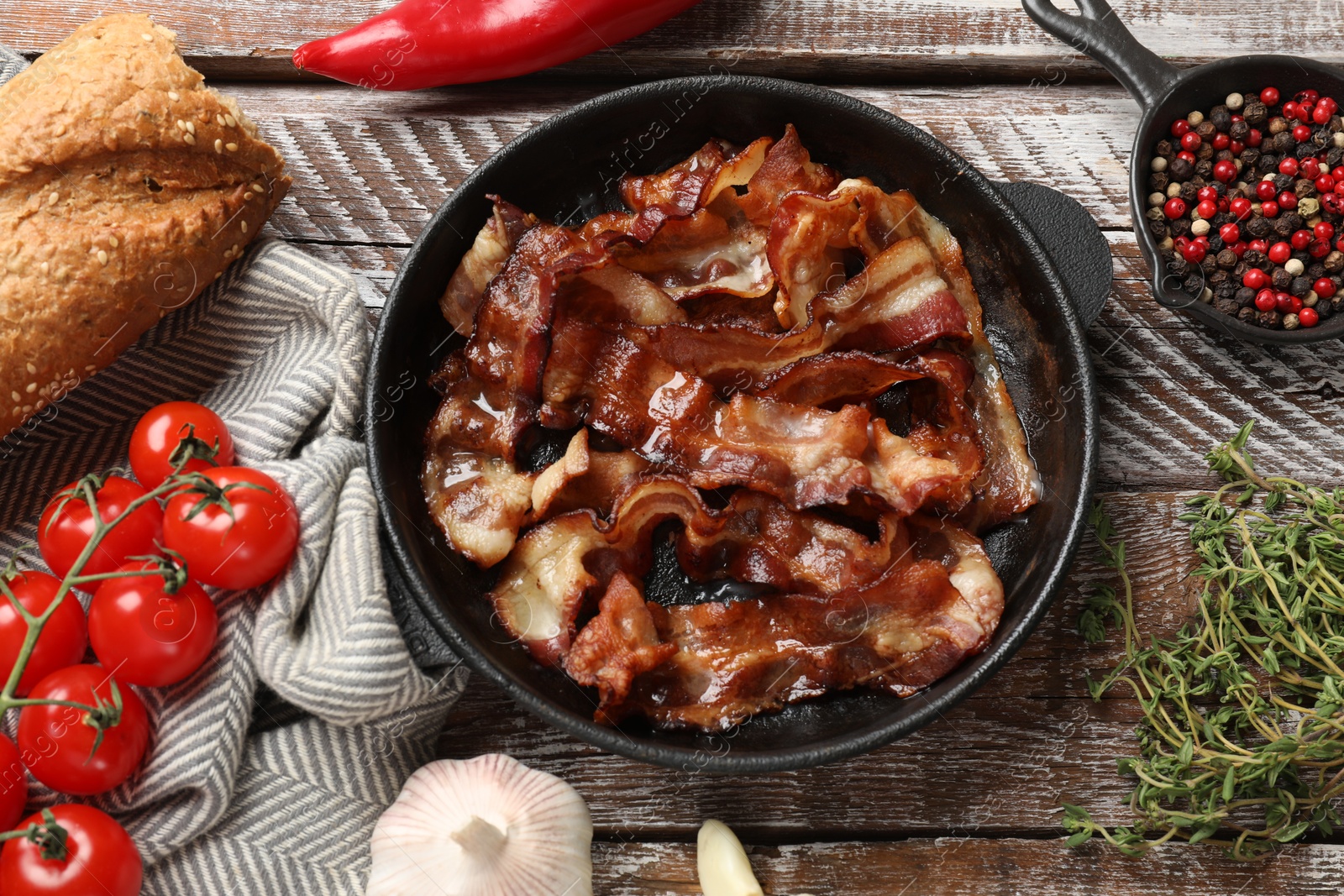 Photo of Delicious bacon slices in frying pan and products on wooden table, flat lay