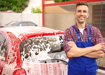 Male worker standing near vehicle covered with foam at car wash