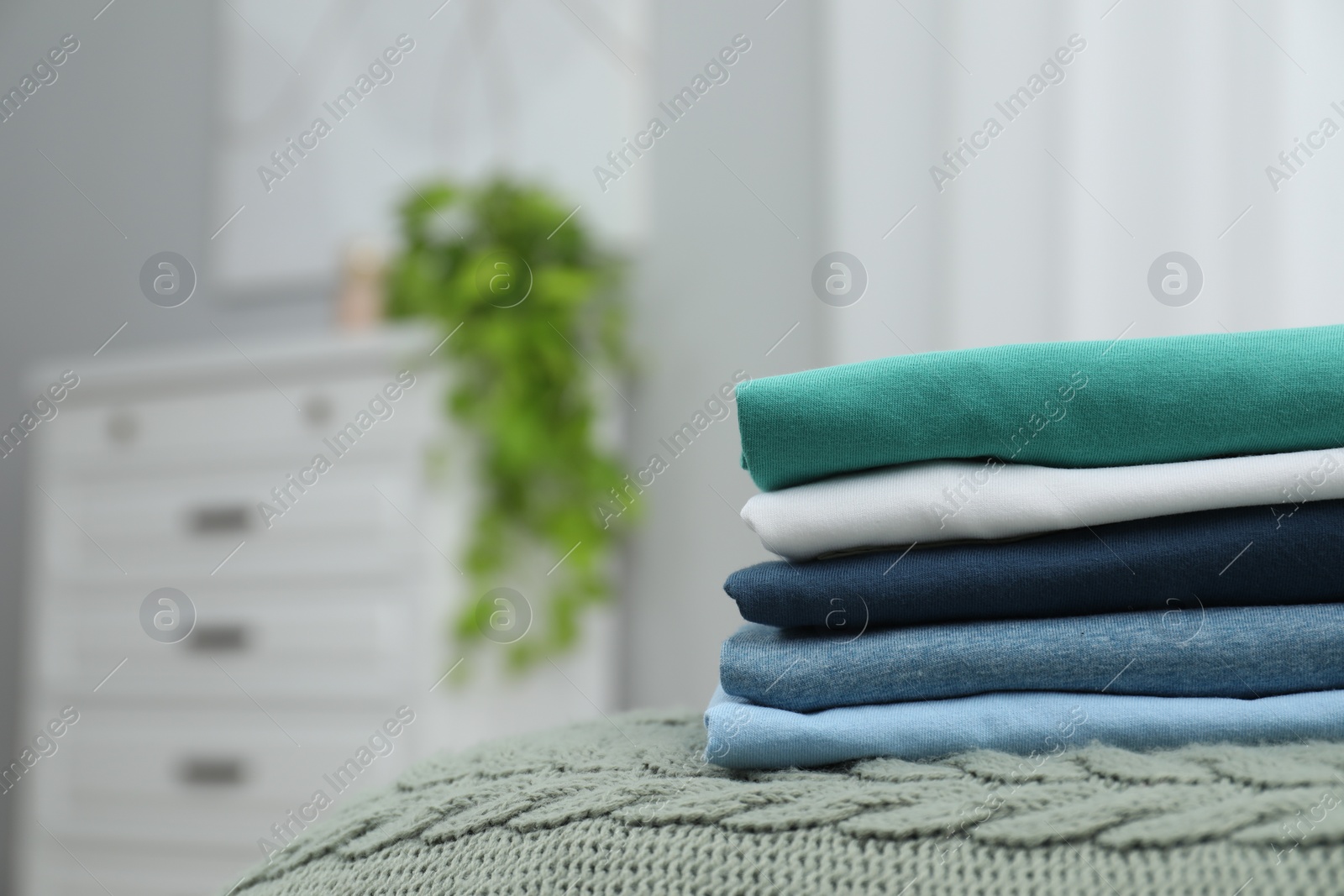Photo of Sorting and organizing. Stack of different folded clothes on bed indoors, space for text