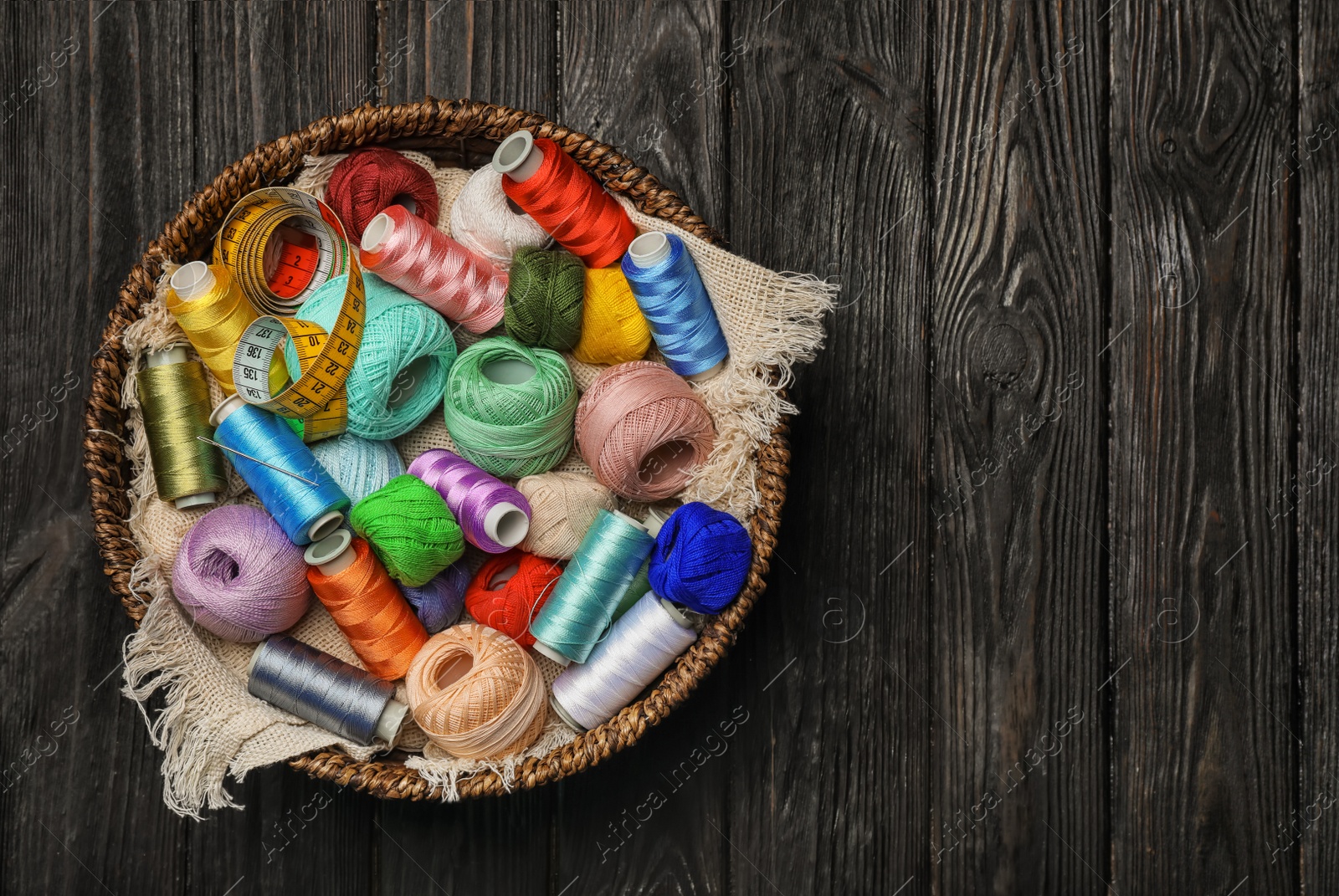 Photo of Basket with color sewing threads on wooden background, top view