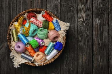 Photo of Basket with color sewing threads on wooden background, top view