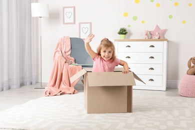 Photo of Cute little girl playing with cardboard box at home