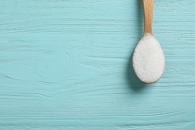 Spoon of white sugar on light blue wooden table, top view. Space for text