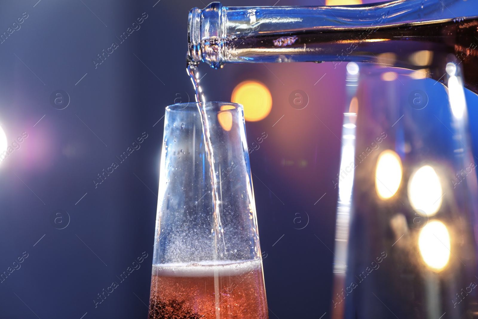 Photo of Rose champagne pouring from bottle into glass on color background, closeup