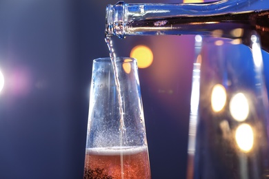 Photo of Rose champagne pouring from bottle into glass on color background, closeup