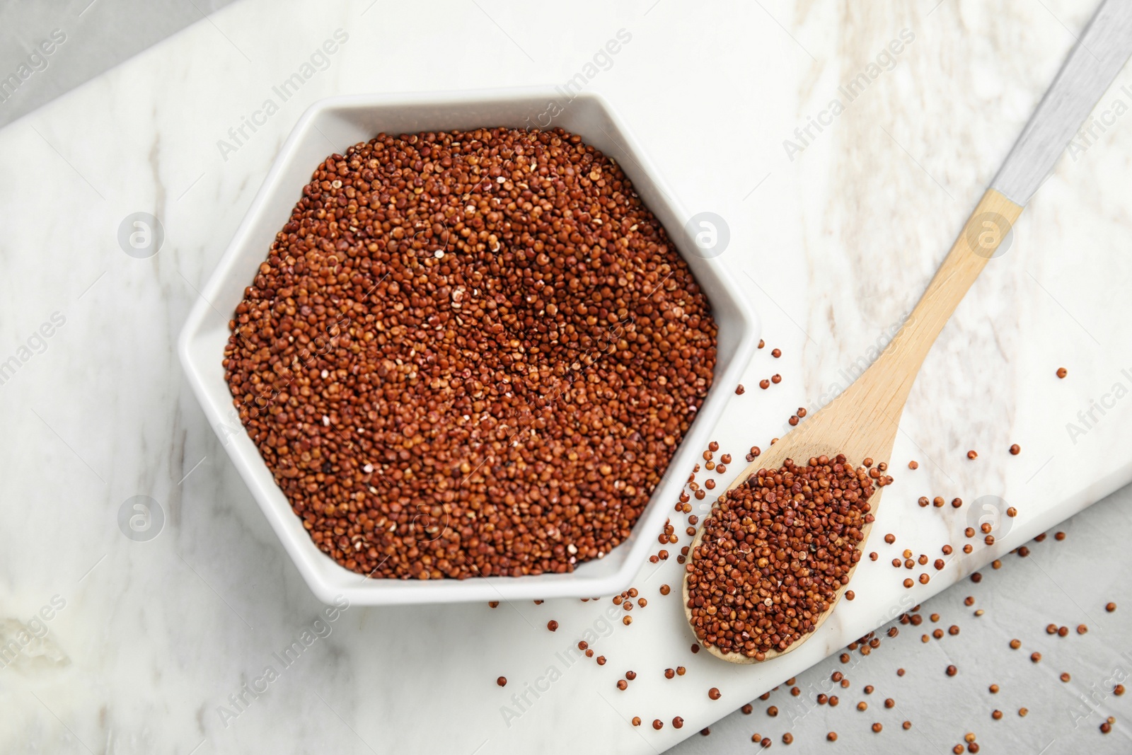 Photo of Bowl and spoon with red quinoa on marble board, top view