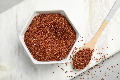 Bowl and spoon with red quinoa on marble board, top view