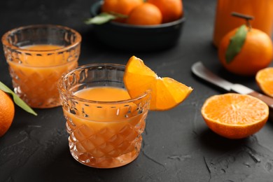 Photo of Tasty tangerine liqueur in glasses and fresh citrus fruits on black textured table