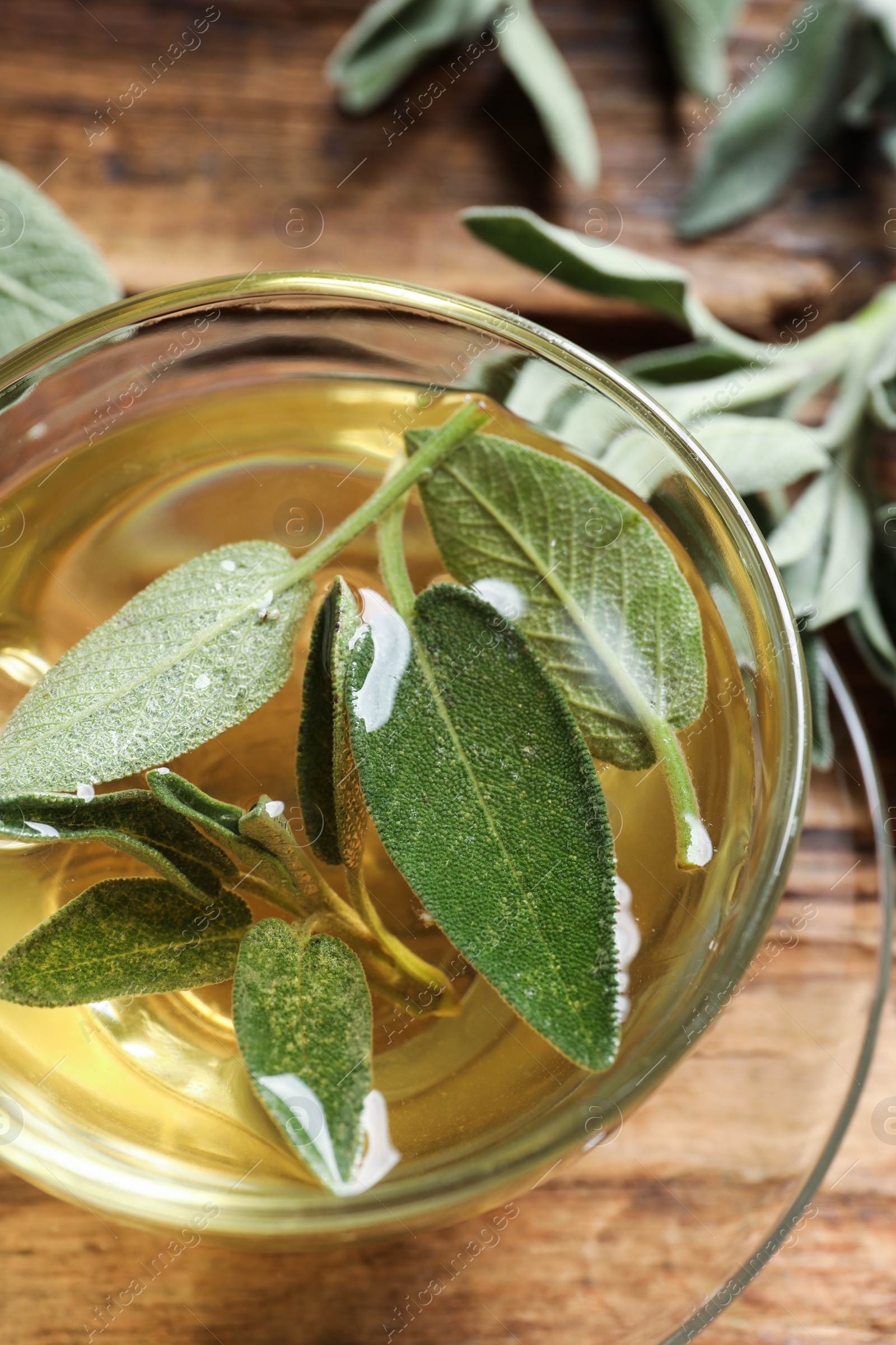 Photo of Cup of aromatic sage tea with fresh leaves on wooden table, closeup