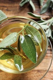 Photo of Cup of aromatic sage tea with fresh leaves on wooden table, closeup