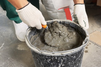 Worker with trowel mixing cement in bucket indoors, closeup