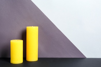 Photo of Decorative wax candles on table against color background