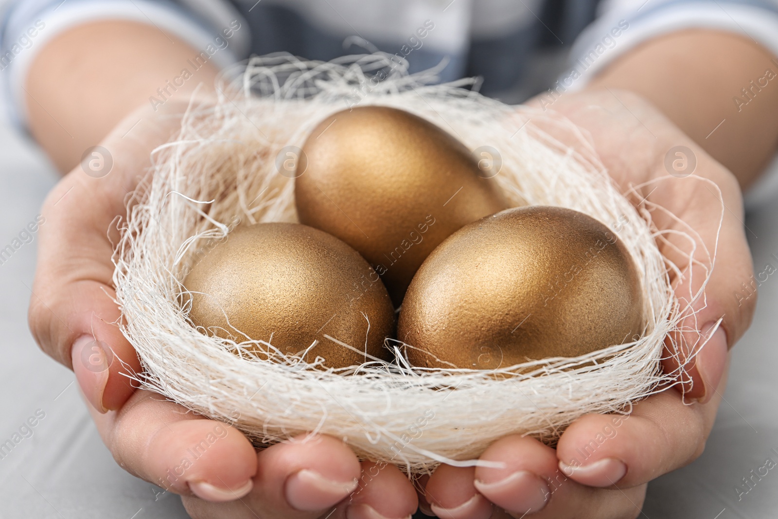 Photo of Woman holding nest with golden eggs over table, closeup
