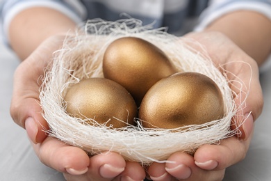 Woman holding nest with golden eggs over table, closeup