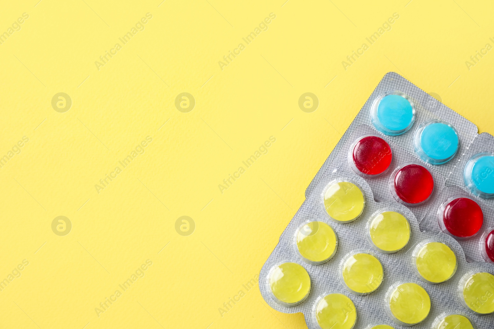 Photo of Cough drops in blisters on yellow background, top view. Space for text