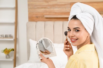 Beautiful woman with mirror applying makeup in bedroom