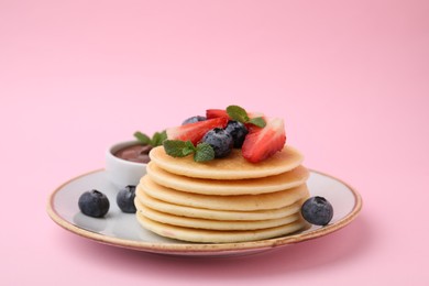 Photo of Delicious pancakes with strawberries, blueberries, and chocolate sauce on pink background, closeup