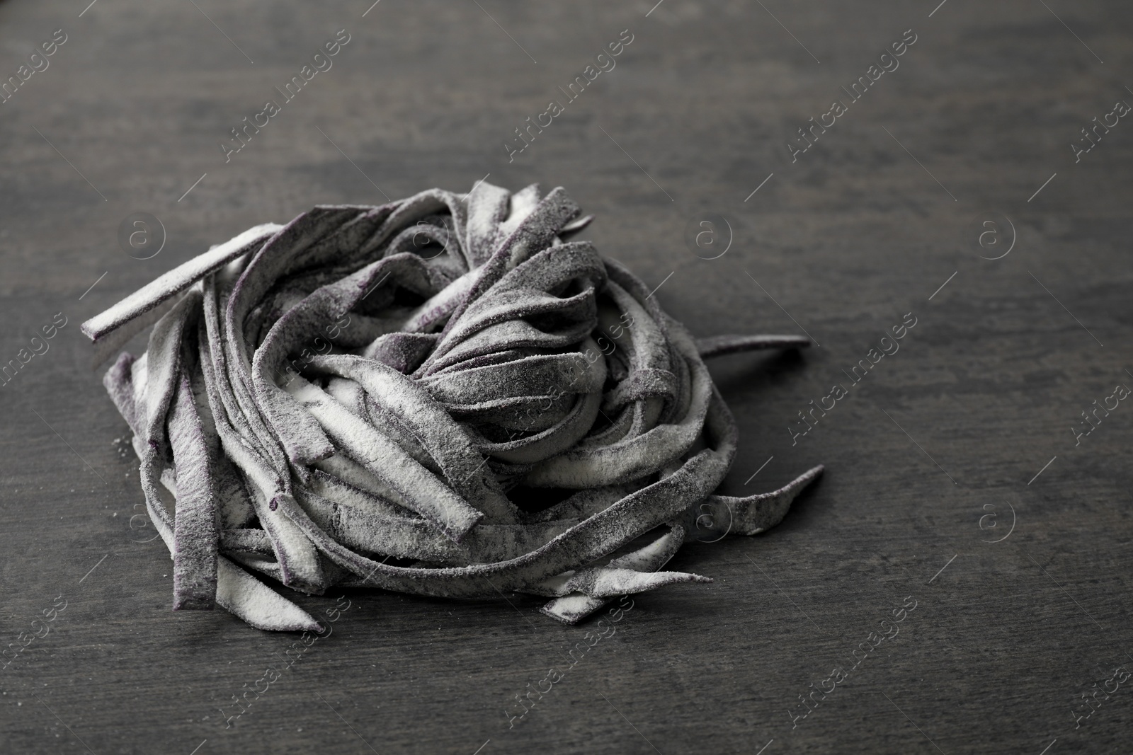 Photo of Rolled pasta painted with food coloring on dark grey table, closeup. Space for text