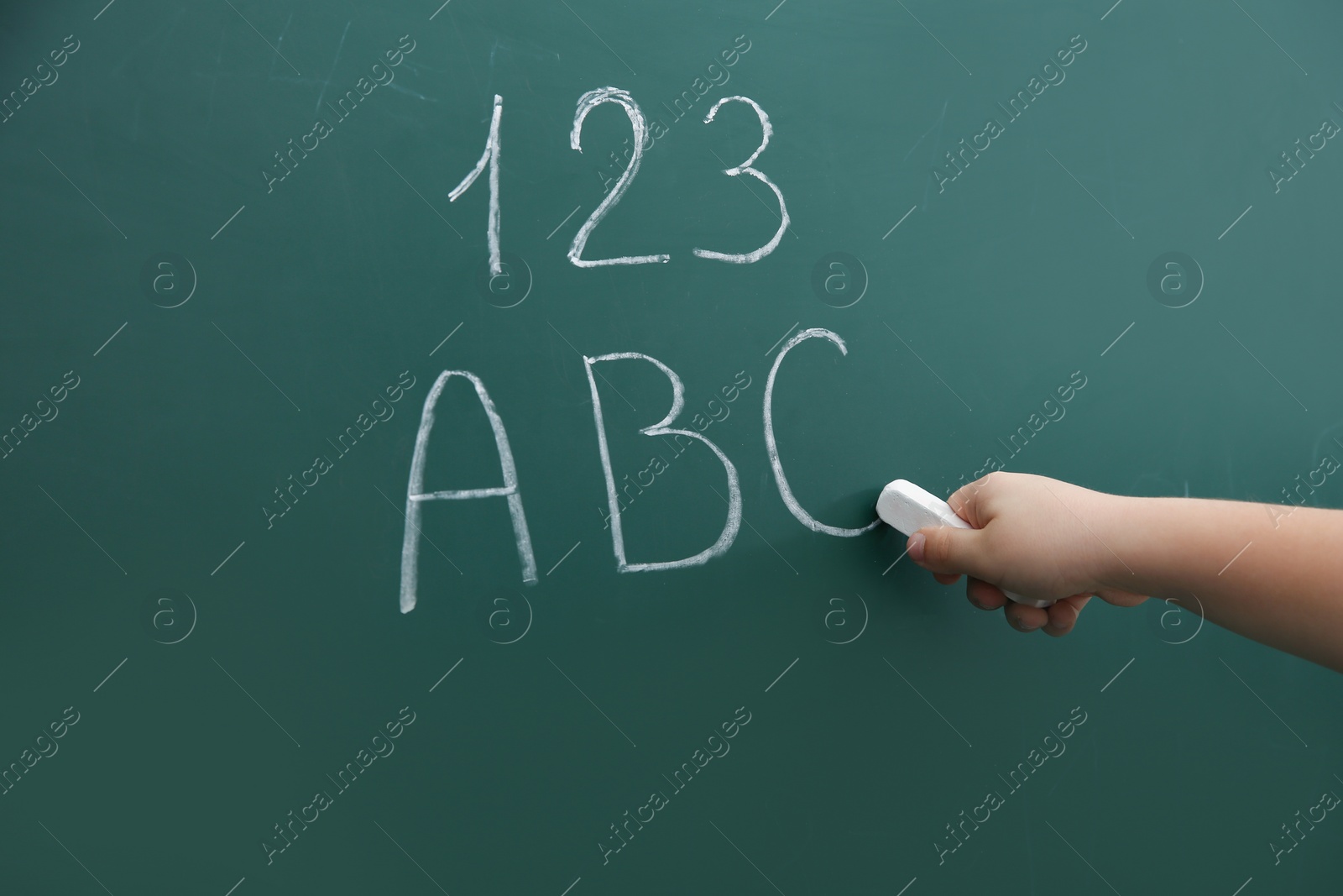 Photo of Little child writing letters and numbers on chalkboard, closeup