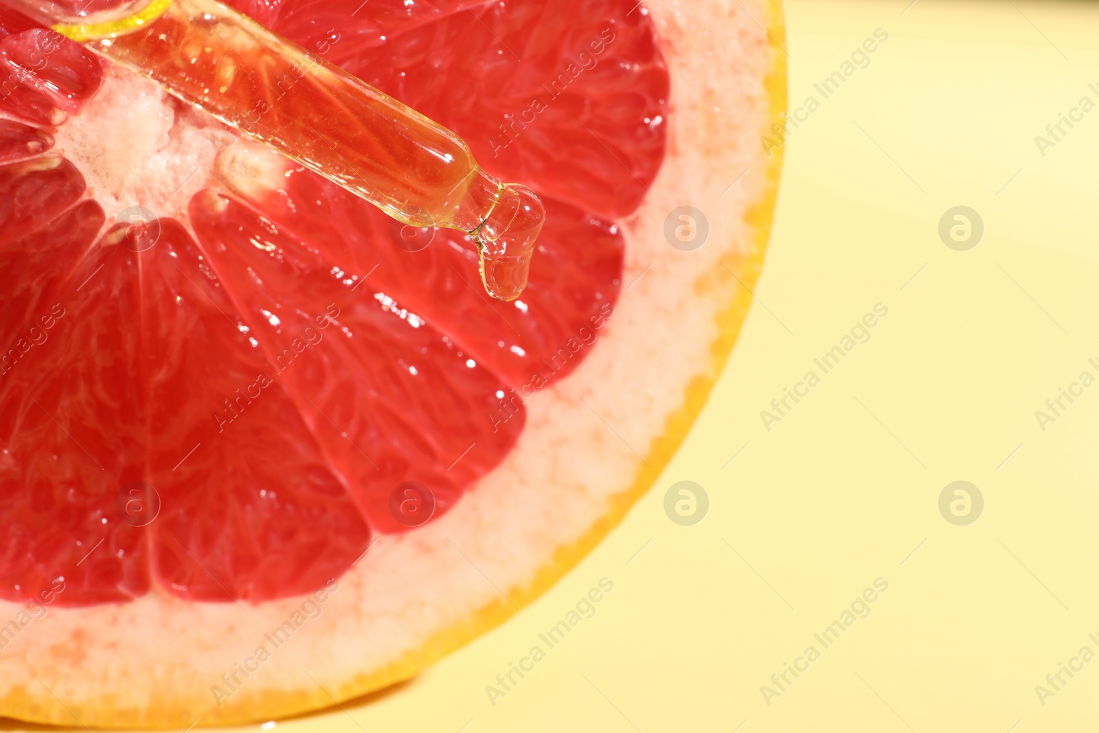 Photo of Dripping cosmetic serum from pipette onto grapefruit slice against yellow background, top view. Space for text