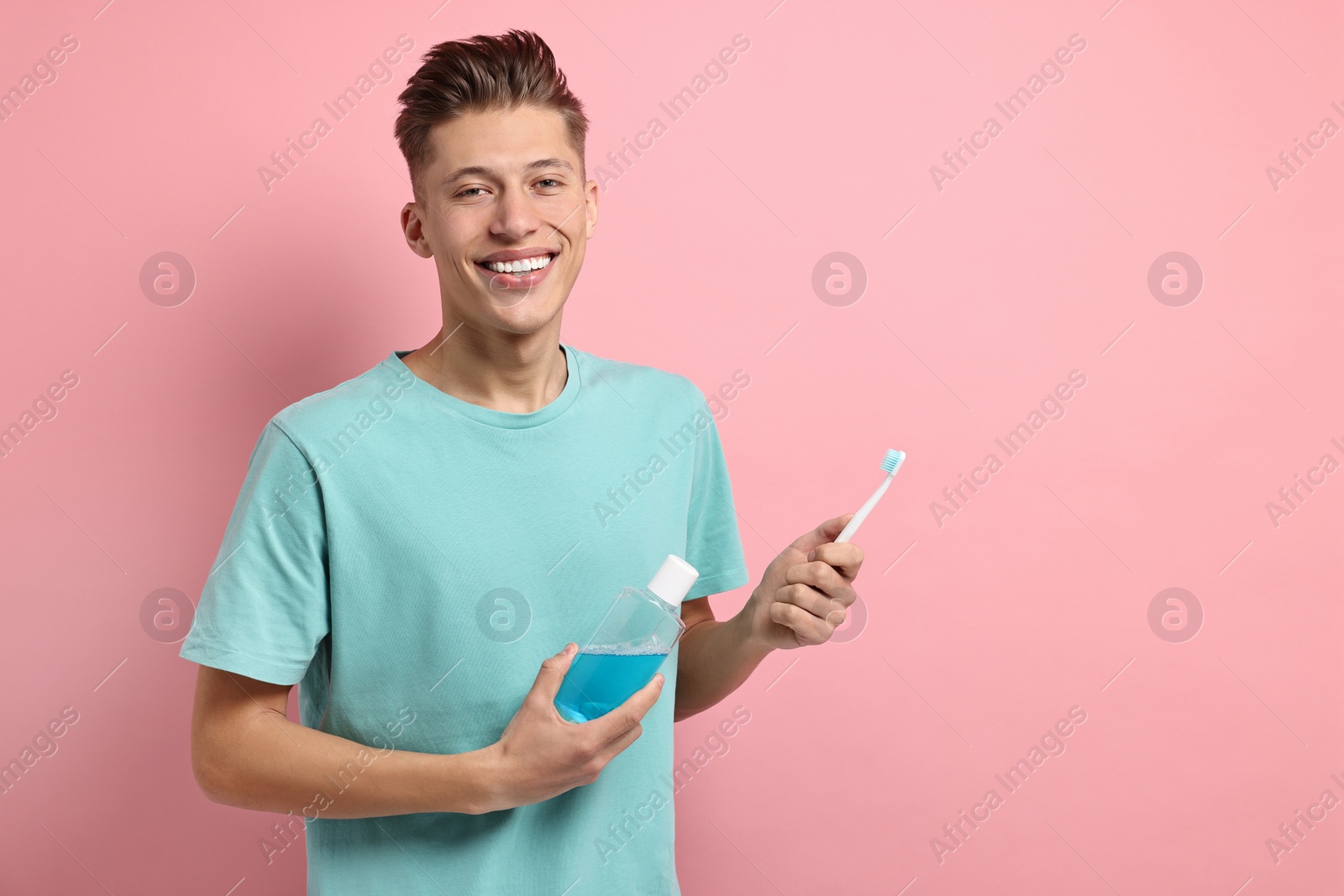 Photo of Young man with mouthwash and toothbrush on pink background, space for text