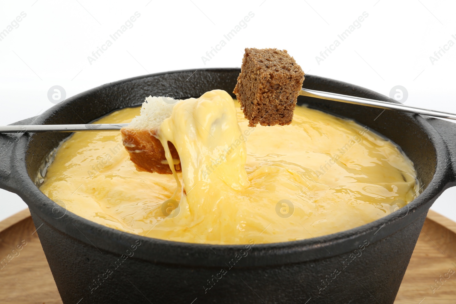 Photo of Pieces of bread above fondue pot with melted cheese isolated on white