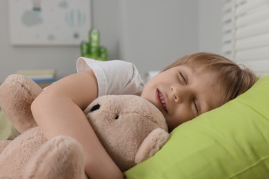 Photo of Little boy snoring while sleeping with teddy bear in bed at home