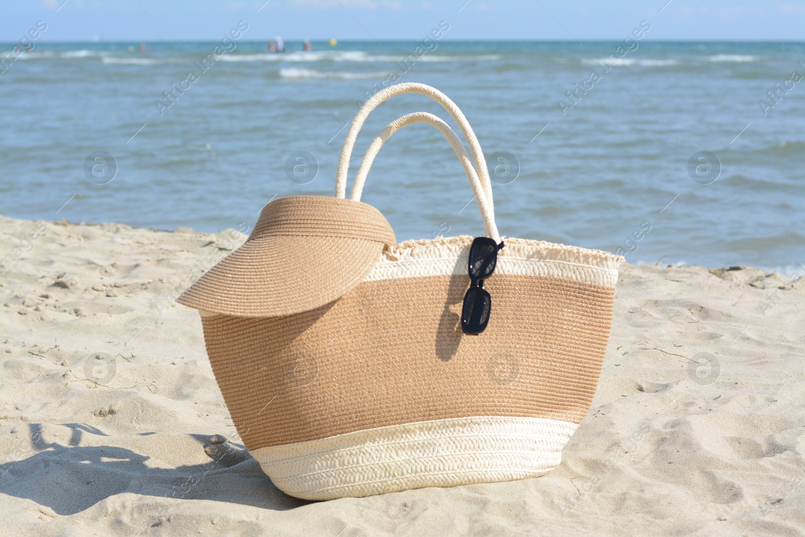 Photo of Stylish straw bag with visor cap and sunglasses on sandy beach near sea