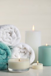 Beautiful spa composition with burning candles and rolled towels on white table