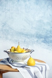 Colander with pears on table against color background. Space for text