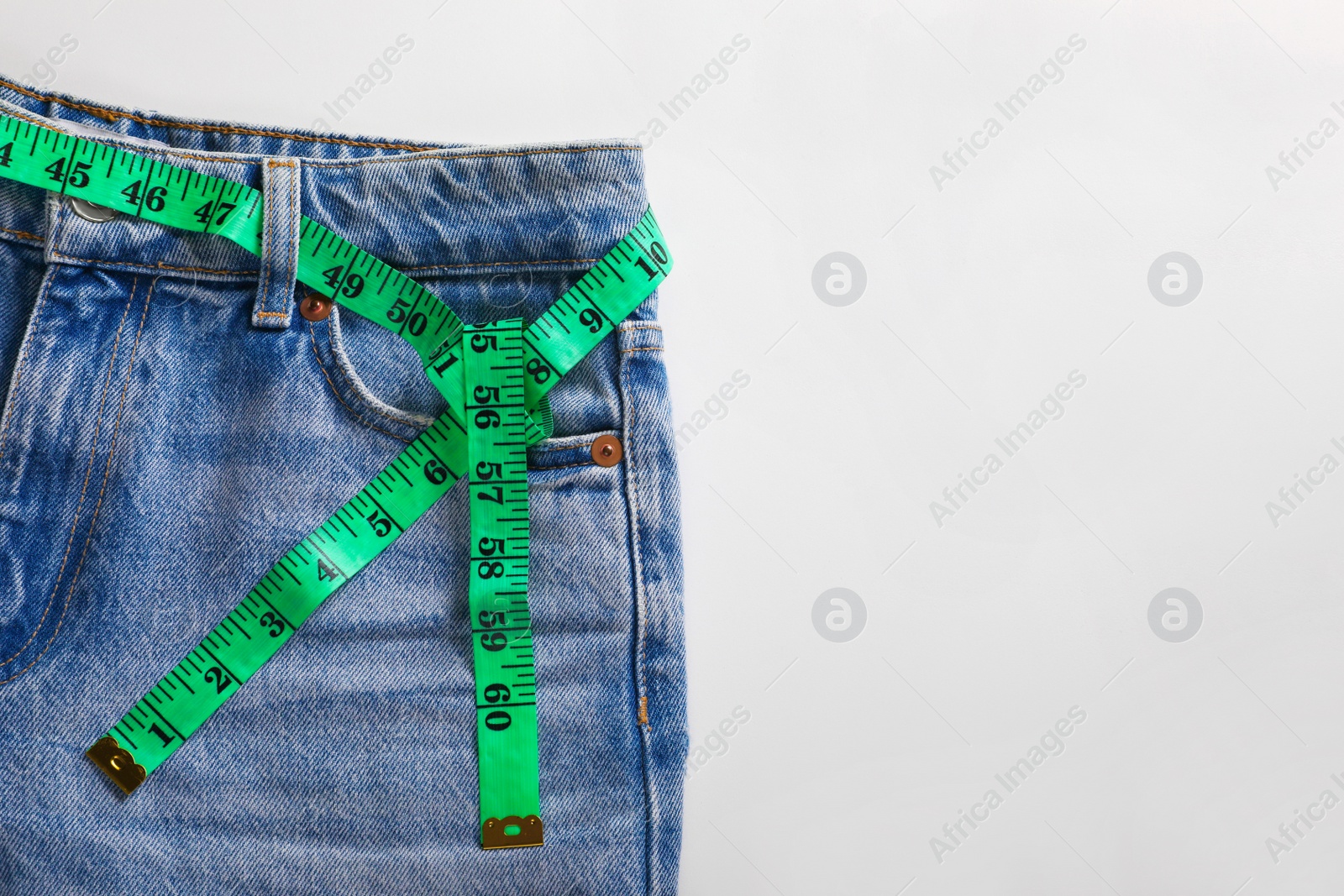 Photo of Jeans with measuring tape on light grey background, top view and space for text. Weight loss concept