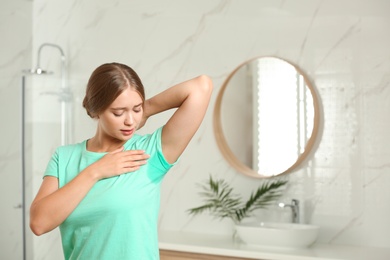 Photo of Young woman with sweat stain on her clothes in bathroom. Using deodorant