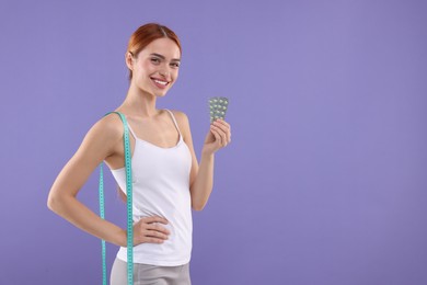 Photo of Happy young woman with pills and measuring tape on purple background, space for text. Weight loss