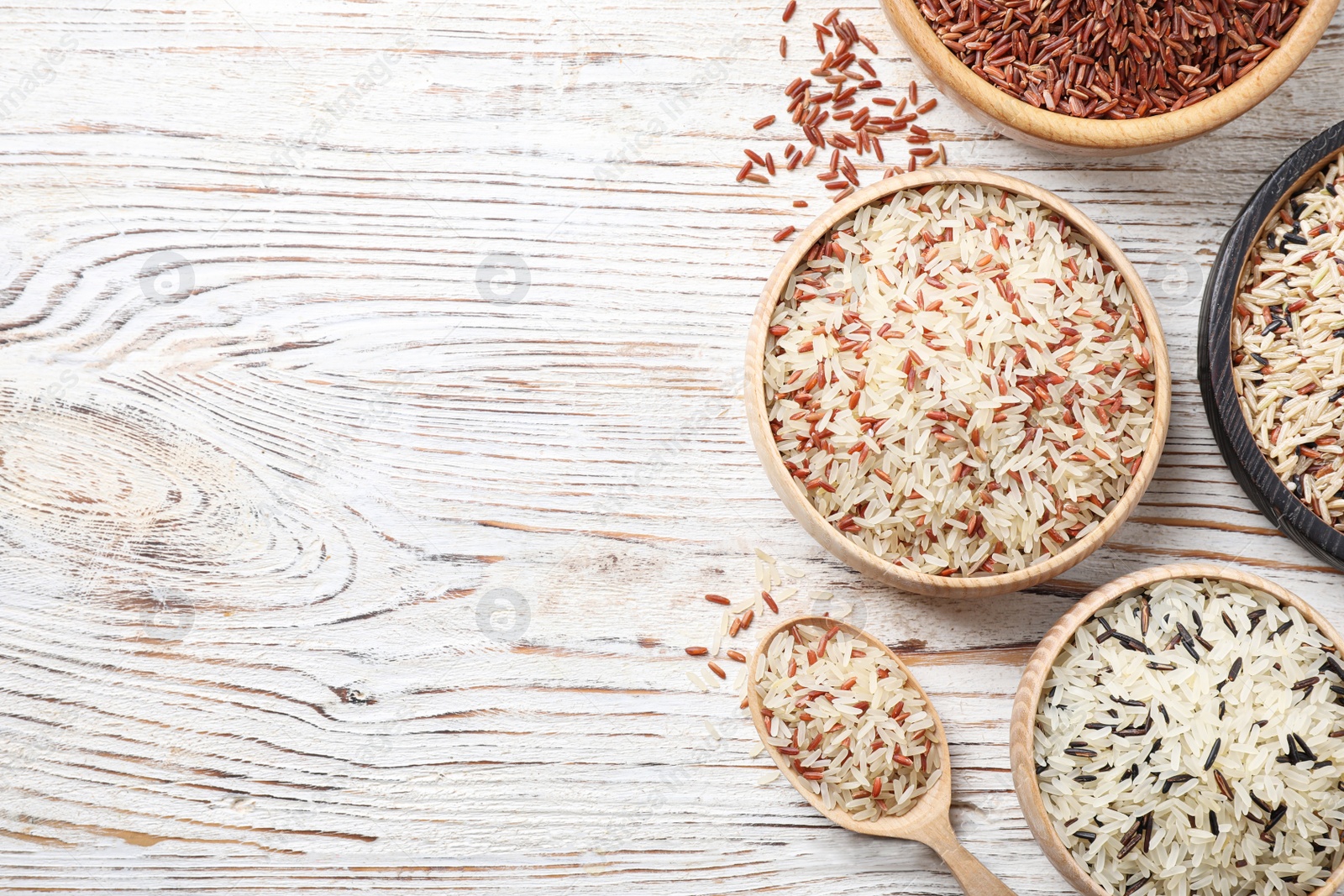 Photo of Different sorts of rice on white wooden table, flat lay. Space for text