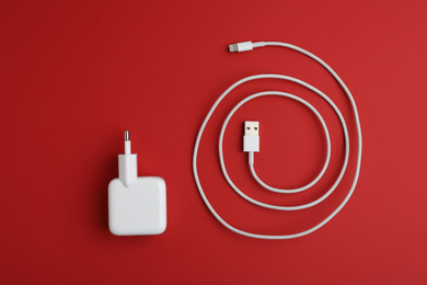 Photo of USB charge cable and adapter on red background, flat lay. Modern technology