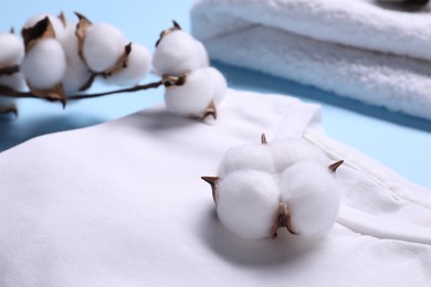Photo of Cotton branch with fluffy flowers and white t-shirt on light blue background, closeup