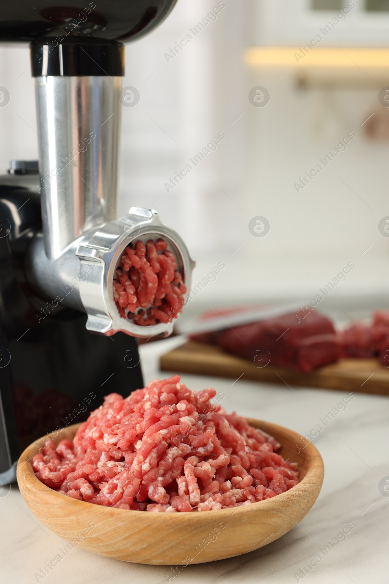 Photo of Electric meat grinder with minced beef on white marble table indoors